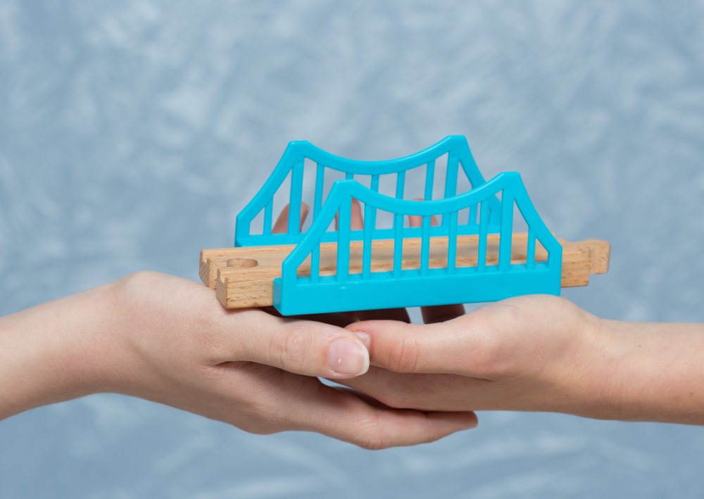 Zwei Hände halten ein Spielzeugeisenbahnbrücke